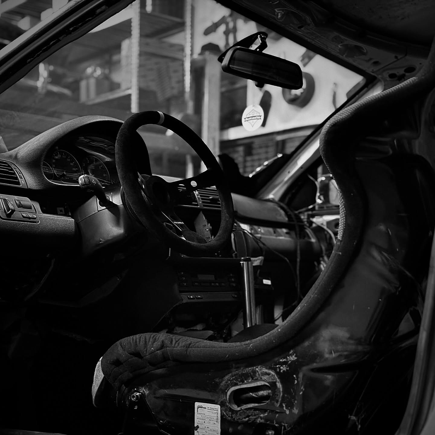 Ausgeräumter Innenraum eines BMW E46 mit Momo-Lenkrad und Recaro-Schale, schwarz-weiß