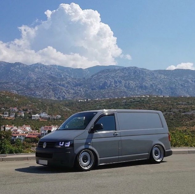 Grauer VW T5 Transporter auf Luftfahrwerk vor Bergen am Meer